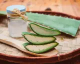 Tranches d'aloe vera sur une cuillère en bois, prêtes à apaiser un coup de soleil. Gel d'aloe vera dans un petit pot à côté.