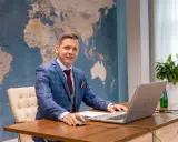 Mężczyzna w garniturze przy biurku z laptopem, na tle mapy świata. Tak wyglądają studia doktoranckie w dzisiejszych czasach – globalne spojrzenie i praca z technologią.