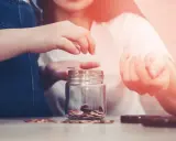 Dwie osoby wrzucają monety do słoika, oszczędzając na przyszłość. Zastanawiasz się, ile wynoszą alimenty na studenta?