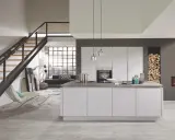 Cuisine moderne avec îlot central blanc. Le mur gris foncé contraste avec les meubles blancs et le bois de chauffage.