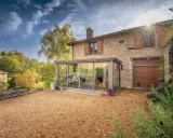 Maison en pierre avec véranda moderne, illustrant la différence entre véranda et extension. Le soleil brille sur le paysage verdoyant.
