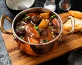 Herzhaftes Chili con Carne in Kupfertöpfchen, mit Kartoffeln, Karotten und Erbsen, serviert mit Baguette.