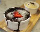 Pyszny, gorący lava cake z mikrofali, posypany cukrem pudrem i udekorowany truskawkami. Obok porcja lodów waniliowych.
