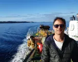 Uomo su nave, con mare e terra all'orizzonte. Un vero oceanografo significato, immerso nella sua ricerca.