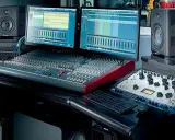 Station de mixage audio avec deux écrans, enceintes, casque et console de mixage.