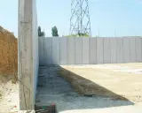 Construcción de muros de contención de hormigón prefabricados, con una torre de alta tensión al fondo.