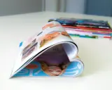 Ein aufgeschlagenes Magazin, das wie ein Herz geformt ist, liegt auf einem Tisch. Im Hintergrund stapeln sich weitere Ausgaben der aero zeitschrift.