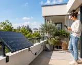 Une femme consulte sa tablette sur un balcon, à côté d'un panneau solaire plug and play installé sur la rambarde.