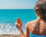 Bambina sulla spiaggia applica crema solare, disegnando un sole e onde sulla schiena. Un modo per non abbronzarsi e proteggersi.