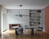 Sala da pranzo moderna con tavolo ovale, sedie imbottite e libreria a giorno. Le pareti grigio luminoso creano un'atmosfera sofisticata.