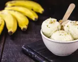 Delicioso helado de plátano cremoso, adornado con nueces, junto a racimos de plátanos frescos sobre una mesa de madera rústica.