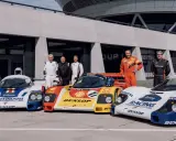 Fünf Rennfahrer stehen stolz neben ihren Porsche-Rennwagen der Gruppe C.