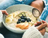 Schüssel mit Haferflocken, Bananen, Blaubeeren und Mandelsplittern. Ein Löffel wartet darauf, die gesunde Mahlzeit zu genießen, die nicht dick machen muss.