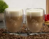 Zwei Latte Macchiato im Glas, umgeben von Kaffeebohnen. Ein typischer Latte Macchiato hat ca. 250-300 ml.