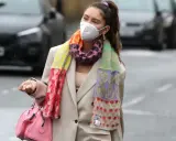 Iris Law, con mascarilla y bufanda multicolor, camina por la calle con un bolso rosa.