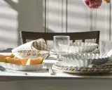 Ett dukat bord med en fin servis, frukt och blommor. Vackra vita skålar med vågiga kanter och glas med textur.
