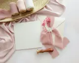 Eleganckie zaproszenie ślubne z różową wstążką i pieczęcią. W tle złota taca z rolkami wstążek. Zastanawiasz się, ile wczesniej zaprasza się na slub?
