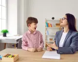 Chłopiec z otwartymi ustami wykonuje ćwiczenia podniebienia miękkiego z logopedą.