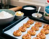 Douze biscuits dorés en forme de rose des sables sur une plaque de cuisson, entourés d'ingrédients pour la pâtisserie.
