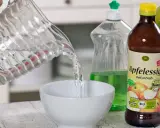 Wasser wird in eine Schüssel gegossen, um eine Fruchtfliegenfalle zu bauen. Apfelessig und Spülmittel sind bereit.