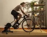 Frau trainiert auf einem Heimtrainer, was ist spinning? Sie tritt kräftig in die Pedale, während im Hintergrund ein Regal mit Pflanzen und Büchern steht.