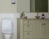 Ett modernt badrum med toalett och ett grönt badrumsskåp med mässingsdetaljer.