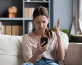 Zirytowana kobieta próbuje włączyć internet w telefonie, gestykulując z frustracją.