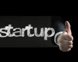 Słowo "startup" napisane kredą na czarnym tle, obok kciuk w górę. To symbol sukcesu w biznesie.