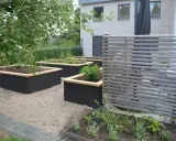 Snygga svarta odlingslådor med träkant ger inspiration för en modern trädgård. Planteringar med grönska och en träskärm.