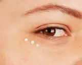 Trois petites perles de crème sont appliquées sous l'œil, montrant comment appliquer contour des yeux pour une peau hydratée.