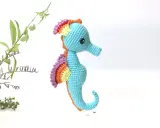 Caballito de mar amigurumi patron gratis. Un adorable caballito de mar tejido a crochet, con aletas arcoíris y cuerpo azul, listo para navegar en tu imaginación.