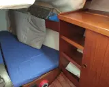 L'intérieur d'un voilier avec une couchette bleue, un coussin gris et des étagères en bois.