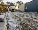 Un seau étiqueté "Allée carrossable" attend sur le chantier. Le gravier est prêt pour la construction de la nouvelle voie d'accès.