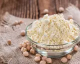 Un bol de farine de pois chiche, riche en protéine, est posé sur un tissu de jute, entouré de pois chiches entiers.