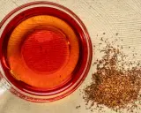 Eine Tasse roter Rooibos Tee neben getrockneten Blättern. Ideal für die Schwangerschaft.