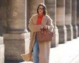 Elegancka kobieta w płaszczu i pomarańczowym golfie, prezentująca modne mom jeans stylizacje zima. Brązowa torebka dodaje szyku.