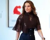 Queen Rania fashion: A woman in a dark brown, floral-patterned top with a high neckline and flared sleeves, paired with a dark skirt.