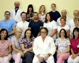 Grupa lekarzy i pielęgniarek w białych fartuchach i kolorowych strojach medycznych, pozująca do zdjęcia.