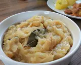 Pyszna, aromatyczna zasmażana kapusta kiszona z liściem laurowym i zielem angielskim, podana w białej miseczce.