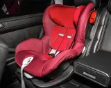 Silla de coche roja en asiento de cuero negro. Las sillas Isofix se pueden poner con cinturón, ofreciendo versatilidad para la seguridad infantil.
