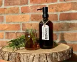 Zutaten für Rosmarinwasser Haare selber machen: frischer Rosmarin, ein Glas mit Flüssigkeit und eine dunkle Flasche mit Pumpspender.