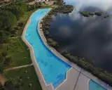 Vista aérea de la piscina natural de Riosequillo, con su agua azul brillante bordeada por césped verde y un lago oscuro.