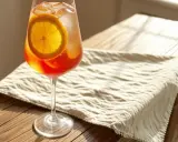 Ein erfrischender Aperol Spritz mit Sekt oder Prosecco, garniert mit einer Orangenscheibe, steht auf einem Holztisch.