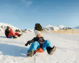 Bambini felici scendono con slittino su pendio innevato. L'altitudine neonati non è un problema per queste avventure invernali.