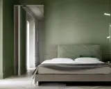 Camera da letto con pareti verde bosco, letto moderno con testiera tessuta e lampada geometrica.