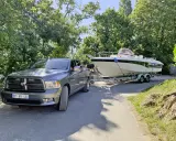 Un pick-up gris est prêt à tracter un bateau de 7m sur sa remorque, sous un ciel bleu et entouré de verdure.
