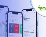 Trzy smartfony pokazują aplikację eToro z wykresami i danymi giełdowymi. Czy eToro jest bezpieczne? Platforma oferuje handel akcjami, kryptowalutami i innymi instrumentami.