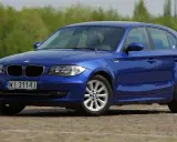 Niebieskie BMW 118i na tle zieleni. Elegancki hatchback z polskimi tablicami rejestracyjnymi WI 3114J.