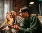 Trzech przyjaciół gra w darmowe gry na PS4, śmiejąc się i rywalizując.
