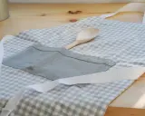 Gotowy fartuch kuchenny w kratkę, z drewnianą łyżką w kieszeni. Idealny poradnik, jak uszyć fartuch kuchenny.